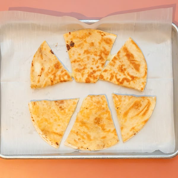 Six triangular quesadilla slices with melted cheese on parchment paper in a metal tray.