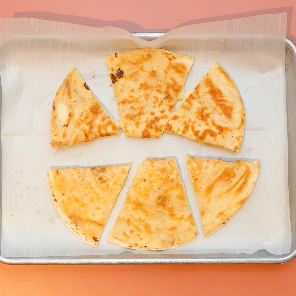 Six triangular quesadilla slices with melted cheese on parchment paper in a metal tray.