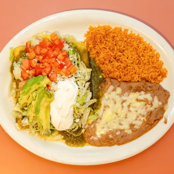 Mexican combination plate with enchiladas, rice, refried beans, avocado, sour cream, and diced tomatoes.