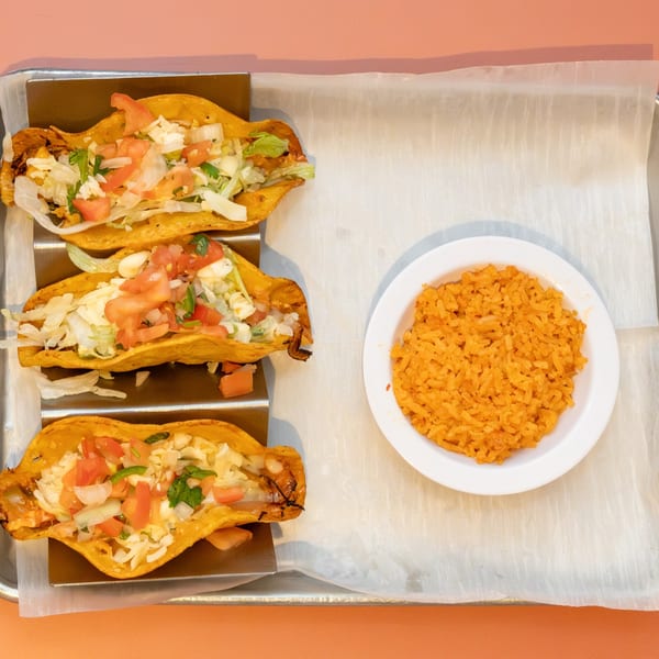 Three crispy tacos filled with lettuce, cheese, and tomatoes, served with a side of orange rice.