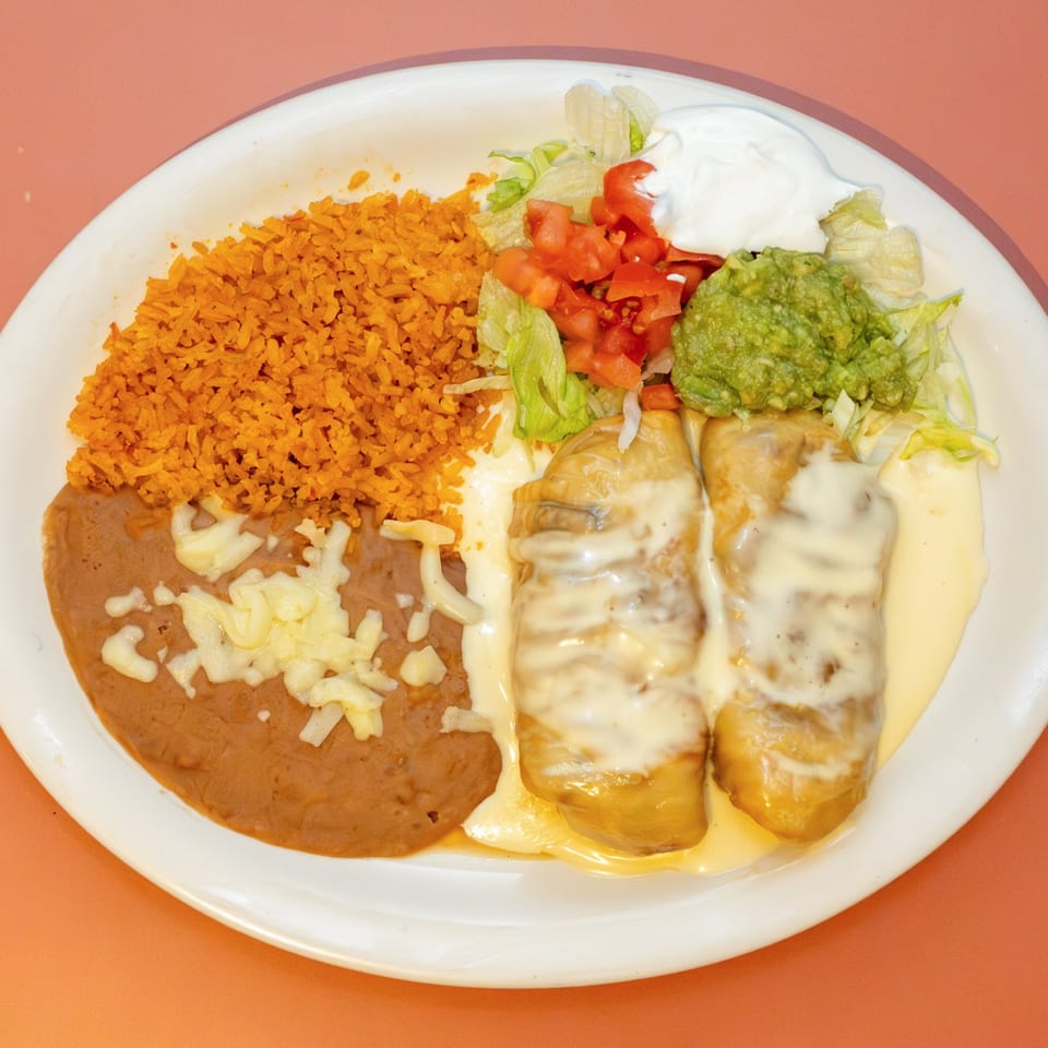 Two cheese-covered burritos with rice, refried beans, lettuce, tomatoes, guacamole, and sour cream.