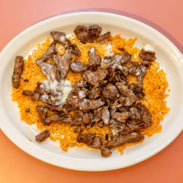 A white oval plate filled with orange rice and topped with steak and white sauce.
